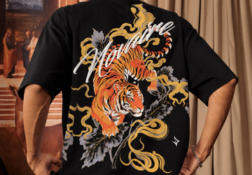 A man wearing a black t-shirt with a large graphic print of a tiger, flames, and the word 'NOVAIRE' on the back, posed in front of a classical painting and beige curtains.